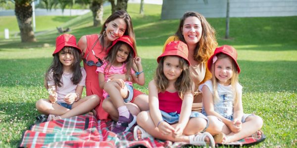Friends enjoying a sunny day picnic on grass with bucket hats and smiles in a Portuguese park.